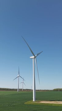 Aerial view approaching wind turbines on a wind farm generating clean and renewable energy on agricultural land with crops in fields and sunny blue sky