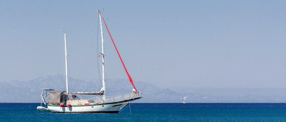 Ultra-wide panoramic seascape featuring a white sailboat on calm turquoise water with distant mountains and extensive copy space for travel themes © vshq
