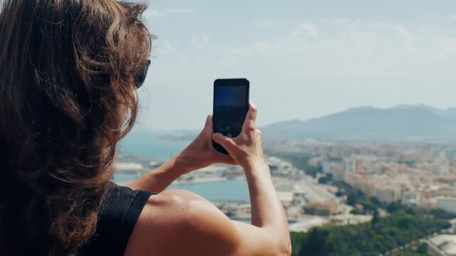 Woman embracing panoramic view of Malaga harbor and cityscape from hilltop viewpoint, capturing memorable travel moments and savoring scenic discovery.