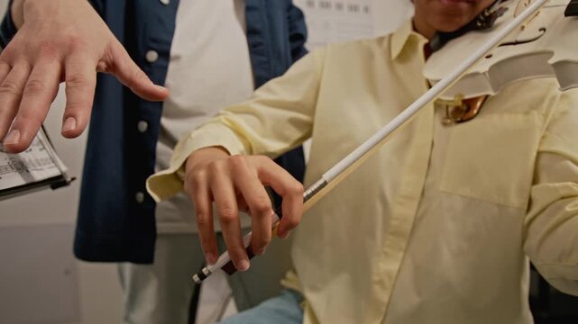 African American teenager learning to hold violin bow during music lesson with Caucasian instructor. Clip for music school commercials and educational marketing campaigns
