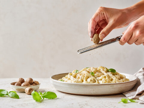 Preparaci&oacute;n de pasta con nuez moscada y albahaca en un plato con mesa clara