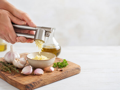 Preparaci&oacute;n de ajo picado con un prensador en la cocina con ingredientes frescos y un fondo claro