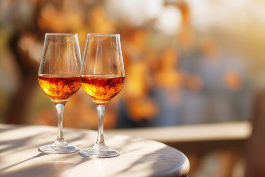aperitif. Simple outdoor bistro setup with two orange wine glasses on a light wood or stone table. Soft sunlight, blurred fall background. No people