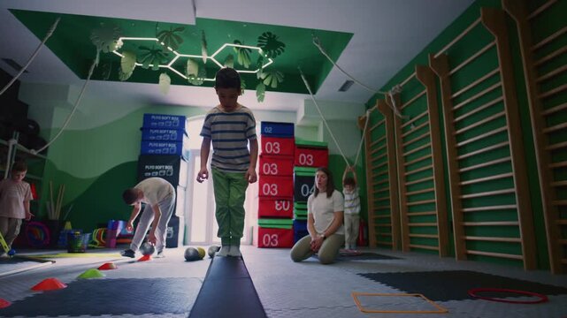A young boy actively participates in a kids fitness class, jumping onto a plyo soft box. Children engage in various exercises, promoting a healthy and active lifestyle.