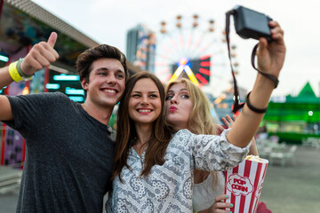 Fototapeta premium Three friends taking a selfie at a carnival with a Ferris wheel.