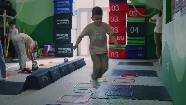 Young children participate in various fitness exercises and agility drills in a colorful gym. These active kids are developing coordination and physical skills through engaging activities.
