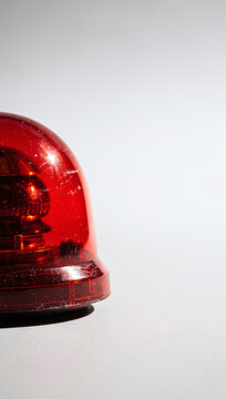 A red emergency flasher siren light stands on a surface against a light background