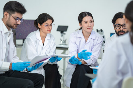 Two scientists reviews a sample card and tablet at a laboratory discussion, wearing white coats and gloves, supporting innovation and teamwork, highlighting science and technology.