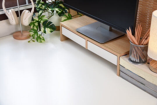 Minimal desktop workspace with computer monitor, wooden monitor stand, headphones, indoor plants and office accessories, featuring clean copy space for design projects