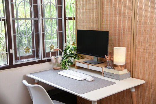 Modern contemporary home office workspace with computer monitor, wooden accessories, indoor plants and natural window light, creating a cozy minimalist interior for remote work