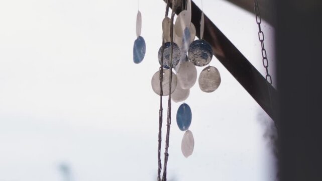 Close-up of a handmade seashell wind chime dangling and moving slowly in a gentle breeze outdoors, creating a peaceful and relaxing atmosphere with its soft, melodic sound