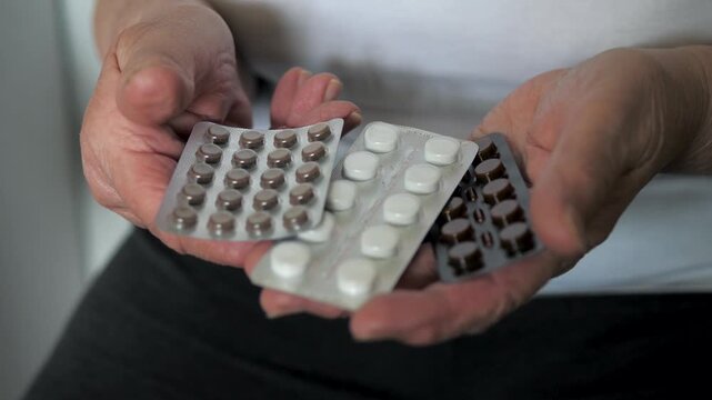 Senior persons wrinkled hands holding various prescription pills in blister packs. Representing health care costs, daily medication regimen and geriatric medicine concepts