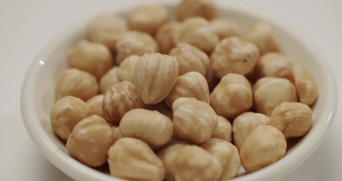 Peeled hazelnuts slowly rotating in a small white bowl isolated on a white background, showing the texture and detail of the healthy nuts, which are a great source of protein and vitamins