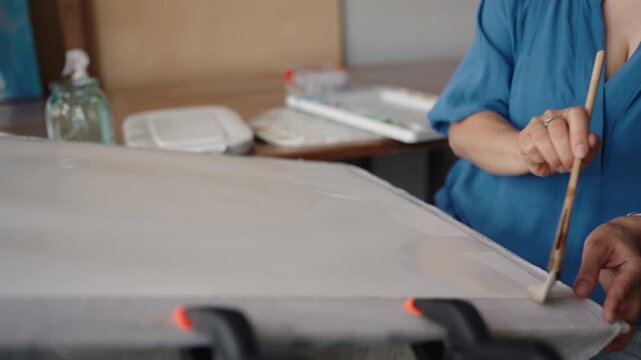 Slow motion video of a professional female artist in her studio applying primer with a large brush to a canvas, preparing the surface for a new painting in a creative and artistic process