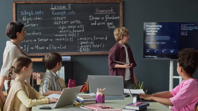Caucasian boy presenting robotics project to multiethnic classmates and female teacher in classroom. Footage ideal for promoting STEM education, coding bootcamps, and modern school curricula