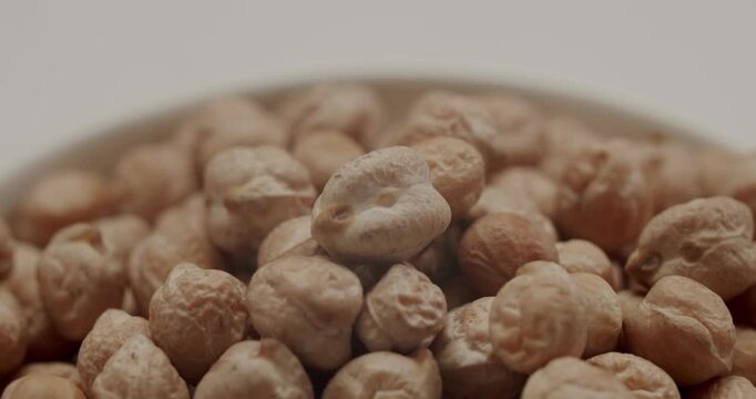 Close-up of a pile of raw, uncooked chickpeas rotating in a bowl on a white background. Healthy, organic legumes rich in protein and fiber, a key ingredient for vegan and vegetarian diets