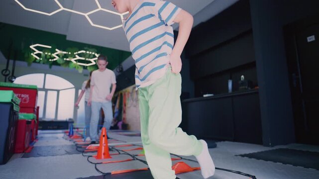 Young children participate in various fitness and agility exercises at an indoor gym. Kids are actively engaged in playful movement and training sessions.