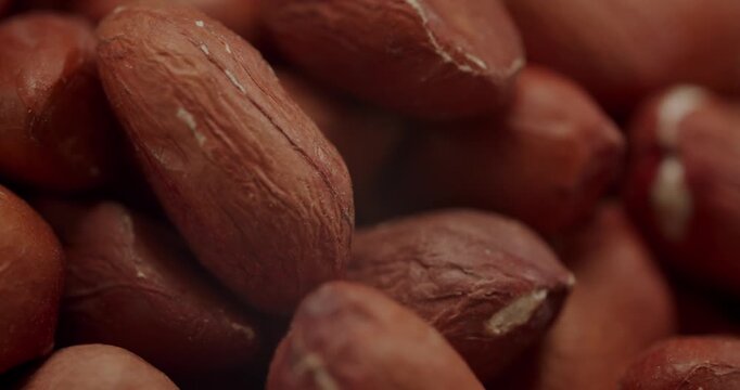 Extreme close up of a pile of peeled peanuts with reddish-brown skin rotating. The nutritious nuts create a textured background for concepts like healthy eating, snacks, and vegan food