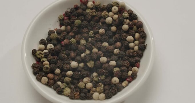 Multicolored peppercorns, including black, white, green, pink varieties, slowly spinning in a detailed macro shot, highlighting the textures and colors of the popular aromatic spice mix. Macro shot