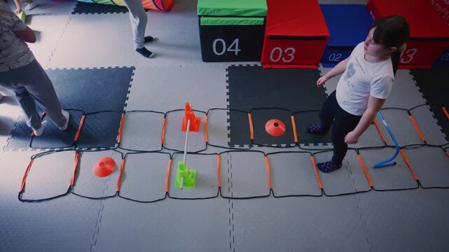 Children are actively participating in a fitness class, navigating an agility ladder with various obstacles. They are developing their physical skills and coordination through engaging exercises.
