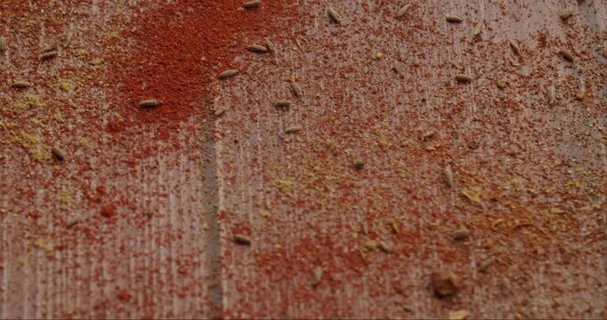 Red paprika powder and cumin seeds getting blown away by a gust of wind from a rustic wooden surface, creating a beautiful and dynamic texture of mixed exotic spices in slow motion