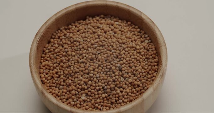 Close-up of yellow mustard seeds slowly rotating inside a natural bamboo bowl, Yellow mustard seeds falling in slow motion creating a dynamic background.