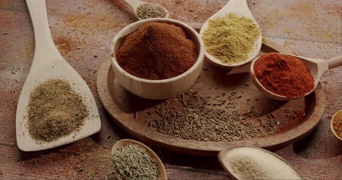 Various colorful and aromatic spices and herbs arranged in wooden bowls and spoons on a rustic table, Various aromatic spices, herbs in wooden bowls and spoons rotating on a rustic wooden background,