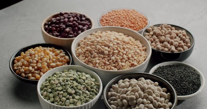 Collection of different types of beans and cereals in bowls rotating on a table. Healthy and nutritious food containing high amounts of fiber and protein, perfect for a vegan diet