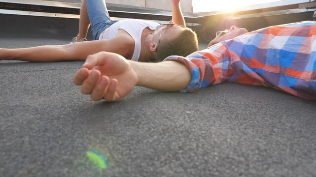 Two young gays lying on roof and smoking with bright sunlight at background. Men resting and enjoying life together. Friends relaxing outdoor at sunset time. Beautiful bottom view Slow mo Close up