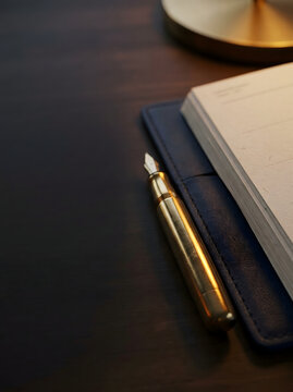 Pluma estilogr&aacute;fica dorada elegante junto a una libreta de cuero abierta sobre escritorio de madera oscuro
