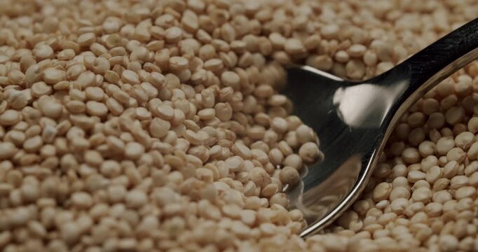 Close-up shot of a shiny metal spoon scooping up a pile of uncooked organic quinoa seeds in super slow motion, highlighting the texture and details of the healthy superfood