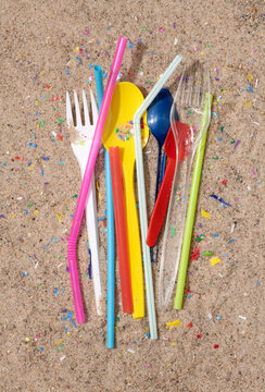 Disposable single use plastic objects and pieces of microplastic on sand, top view.