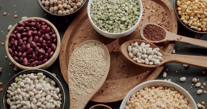 Assortment of raw legumes, pulses, and grains in bowls and spoons, including chickpeas, lentils, peas, quinoa, and beans, arranged on a dark surface, highlighting sources of plant-based protein.