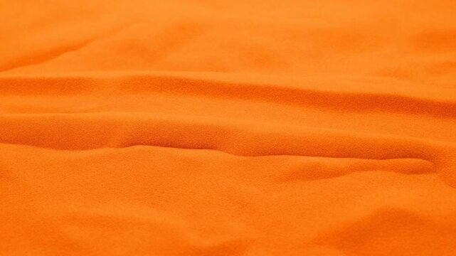 Close-up view of a hand gently pressing and smoothing orange fabric, showcasing texture and movement across three sequential frames in a well-lit setting