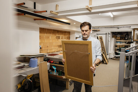 Workshop craftsman holding framed artwork in studio