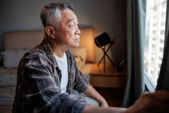 Elderly man gazes out window, lost in thought.