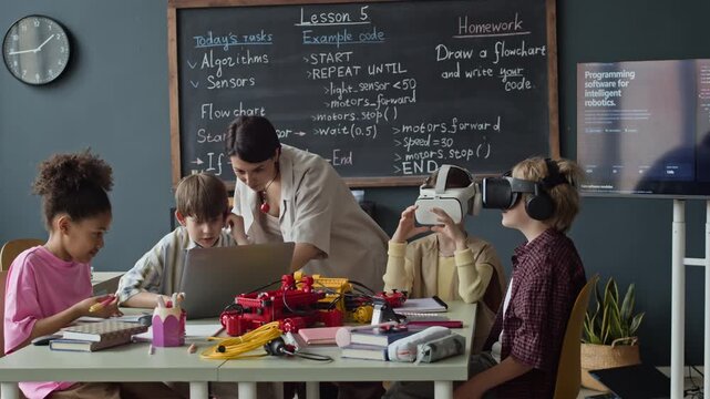 Multiethnic children studying robotics with Caucasian female teacher in classroom, some kids using VR headsets and laptop. Ideal for promoting STEM education and modern school programs