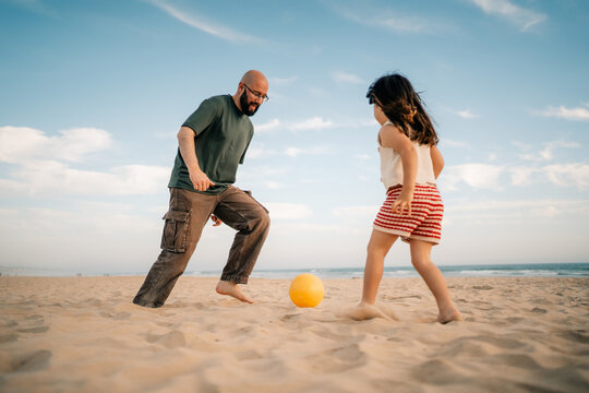 Man and Girl Play With a Ball on the Beach in Daylight
