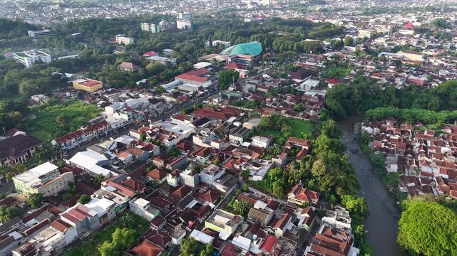 Drone aerial photo over Jember, Indonesia showing dense residential rooftops, a winding river, tree-lined corridors and scattered public buildings, highlighting urban layout, community life
