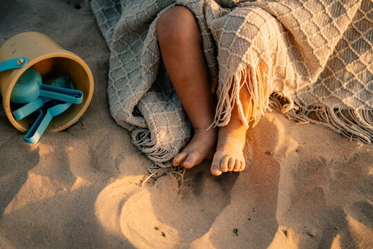 Child Sits on the Sand With a Blanket and Toys in the Evening Sun