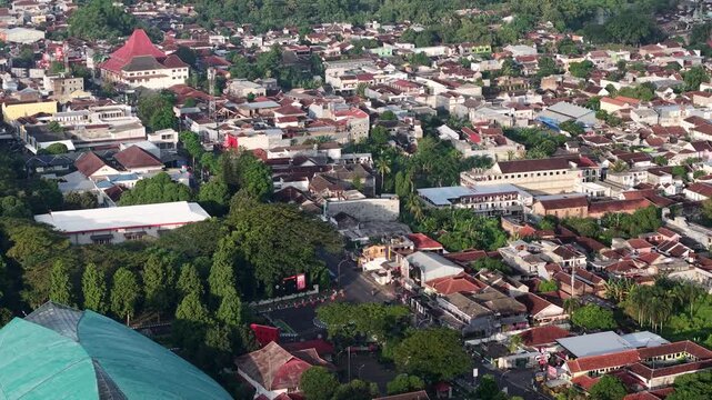 High angle aerial photograph of Jember city showing dense residential rooftops, tree-lined streets and urban greenery, conveying community, everyday life and tropical small-city atmosphere from above
