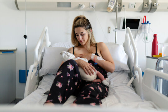 Mother breastfeeding newborn baby in hospital bed