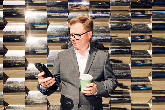 Man With Coffee Looks at Phone in Urban Setting