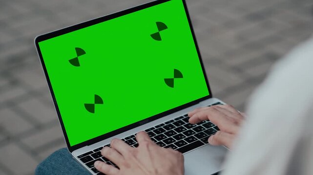 Close up of hands typing on a laptop with green screen outdoors on paved surface