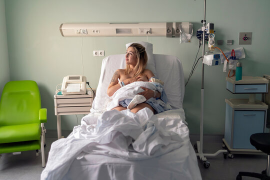 New mother breastfeeding newborn baby in hospital room
