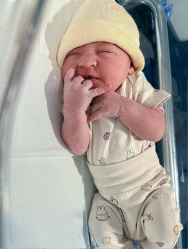 Newborn baby sleeping and discovering tiny fingers in hospital crib