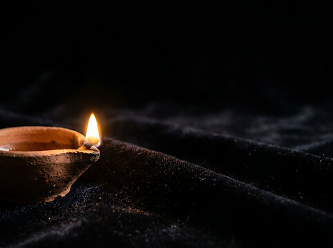 Lit traditional clay diya lamp glowing on dark textured fabric background symbolizing light and hope
