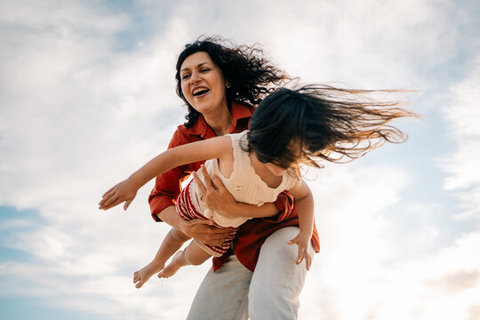 Smiling Woman Holds Child While Playing Outdoors Under Blue Sky