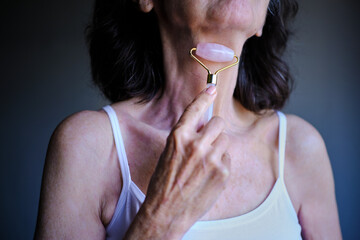 Senior woman using rose quartz jade roller on neck. unrecognizable person © Cristina Garcia