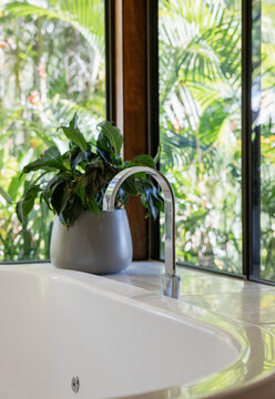 Close up of chrome tap over a spa bath with green lush garden behind